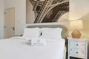 Ein Hotelzimmer mit einem Bett, einem Nachttisch, einer Lampe und einem Wandbild mit dem Eiffelturm.