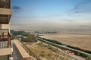 A view of a modern building with a balcony, a desert landscape, and a road with construction barriers. - FIRST CLASS | 1BR | Warm & Stylish Retreat (Dubai Production City)