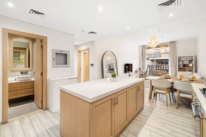 A modern kitchen with a central island, wooden cabinets, and a dining area with a table and chairs. - FIRST CLASS | 1BR | Effortless Elegance (JVC)