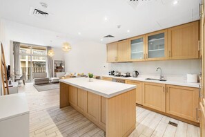 A modern kitchen with wooden cabinets, a large island, and a dining area with a sofa and table. - FIRST CLASS | 1BR | Effortless Elegance (JVC)