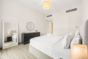 A modern bedroom with a bed, bedside table, dresser, mirror, and a hanging light fixture. - FIRST CLASS | 1BR | Effortless Elegance (JVC)