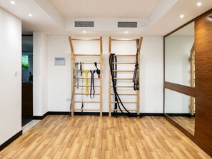 A room with wooden flooring, two wooden wall-mounted racks with exercise equipment, and a large mirror on one wall. - FIRST CLASS | 1BR | Effortless Elegance (JVC)