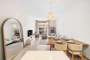 A modern living room with a dining area, a large mirror, and a television. - FIRST CLASS | 1BR | Effortless Elegance (JVC)