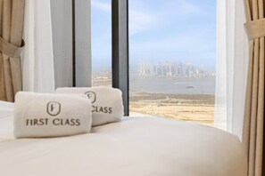A hotel room with a bed, two pillows labeled 'FIRST CLASS,' and a view of a city skyline through large windows. - FIRST CLASS | 1BR | Close to Downtown Attractions (Dubai)