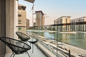 A balcony with two chairs and a table overlooking a river with construction in the background. - FIRST CLASS | 1BR | Cozy Escape | Near Downtown (Meydan)