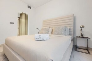Un dormitorio moderno con una cama grande, una mesita de noche con lámpara y una puerta que da a otra habitación.