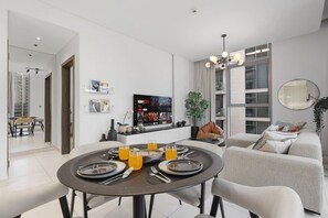 A modern living room with a dining area, a flat-screen TV, and a large window. - FIRST CLASS | 1BR | Cozy Escape | Near Downtown (Meydan)