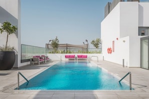 A rooftop swimming pool with a clear blue pool, surrounded by white walls and a glass railing. - FIRST CLASS | 1BR | Chic Retreat | Luxury Escape (JVC)