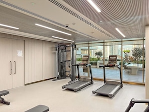 Ein modernes Fitnessstudio mit Laufbändern, Kraftgeräten und einem großen Fenster mit Blick auf die Stadt.
