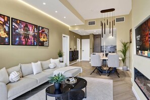 A modern living room with a sofa, a dining table with chairs, and artwork on the walls. - FIRST CLASS | 1BR | Modern Sleek Escape (JVC)