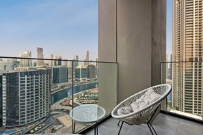 A balcony with a view of a cityscape, a white wicker chair, and a small round table. - FIRST CLASS | 2BR | Tranquil Canal View Haven (Business Bay)