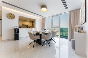 Een moderne eethoek met een ronde tafel en stoelen, een keuken op de achtergrond en een groot raam met uitzicht over de stad.
