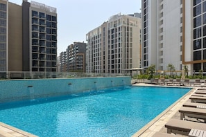 A swimming pool with lounge chairs and a glass railing, surrounded by high-rise buildings. - FIRST CLASS | 1BR | Luxury Escape | Near Downtown (Meydan)