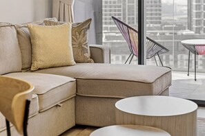 A modern living room with a sectional sofa, a round coffee table, and a city view through large windows. - FIRST CLASS | 1BR | Luxury Escape | Near Downtown (Meydan)