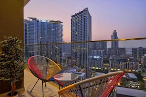 A balcony with a view of high-rise buildings, including one labeled 'SOBHA,' and a glass table with chairs. - FIRST CLASS | 1BR | Luxury Escape | Near Downtown (Meydan)