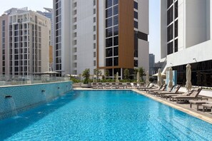 A swimming pool with lounge chairs and umbrellas, surrounded by high-rise buildings. - FIRST CLASS | 1BR | Luxury Escape | Near Downtown (Meydan)