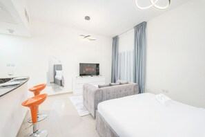Ein modernes Hotelzimmer mit Bett, Fernseher, Schreibtisch und einer Sitzecke mit orangefarbenen Stühlen.