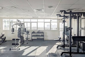 Ein Fitnessstudio mit verschiedenen Trainingsgeräten, einer Hantelbank und großen Fenstern für natürliches Licht.
