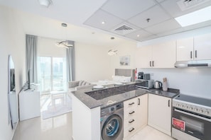 A modern kitchen with a built-in washer, a microwave, and an oven. - FIRST CLASS | Studio | Lavish Cozy Haven (Dubai Sports City)