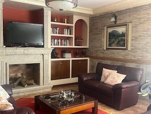 Ein Wohnzimmer mit Kamin, Fernseher, Bücherregal und braunem Ledersofa.
