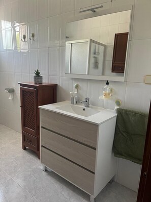 Un baño con lavamanos blanco, tocador de madera y un espejo arriba.