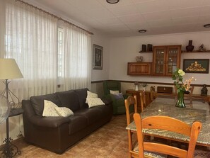 A living room with a dark brown sofa, a dining table with chairs, a lamp, and a vase with flowers. - A villa nestled among vineyards, on an estate with private roads—a true escape to the countryside (Casa los hondos)