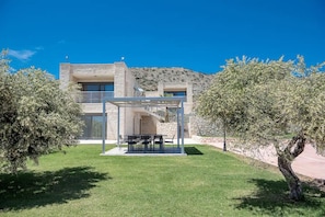 A modern house with a stone facade, a covered outdoor seating area, and a well-maintained lawn. - Elios Estate | 22-Guest Villa with Heated Pool (Marathi)