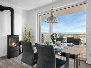 Ein moderner Essbereich mit Kaminofen, einem für zwei Personen gedecktem Esstisch und Meerblick durch große Fenster.
