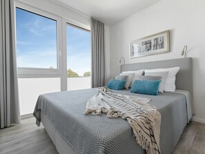 Ein Schlafzimmer mit einem großen Bett, Blick zum Himmel durch ein Fenster und einem gerahmten Bild an der Wand.