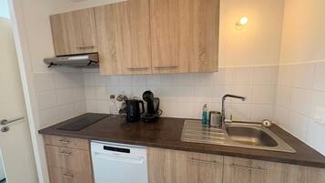 Een kleine keuken met houten kastjes, een vaatwasser, een koffiezetapparaat en een spoelbak.