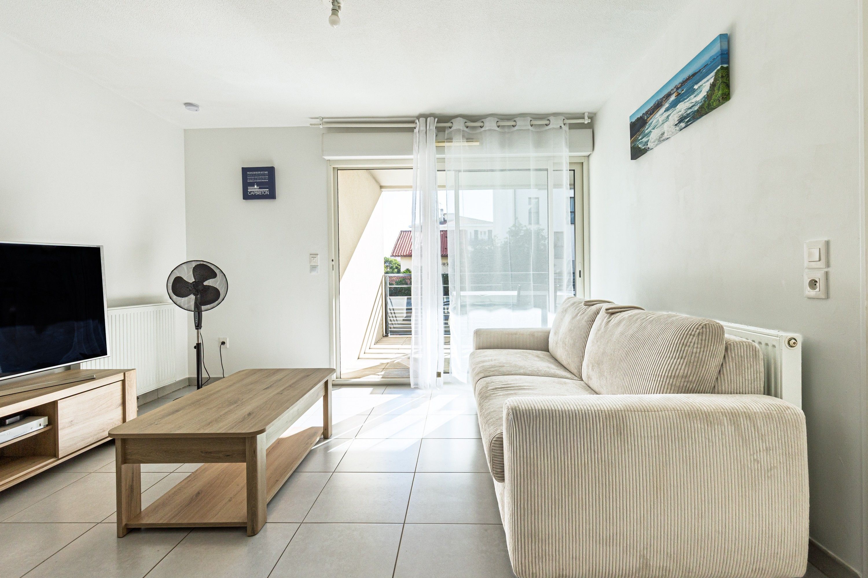 Una sala de estar con una televisión de pantalla plana, una mesa de centro de madera, un sofá y un ventilador.