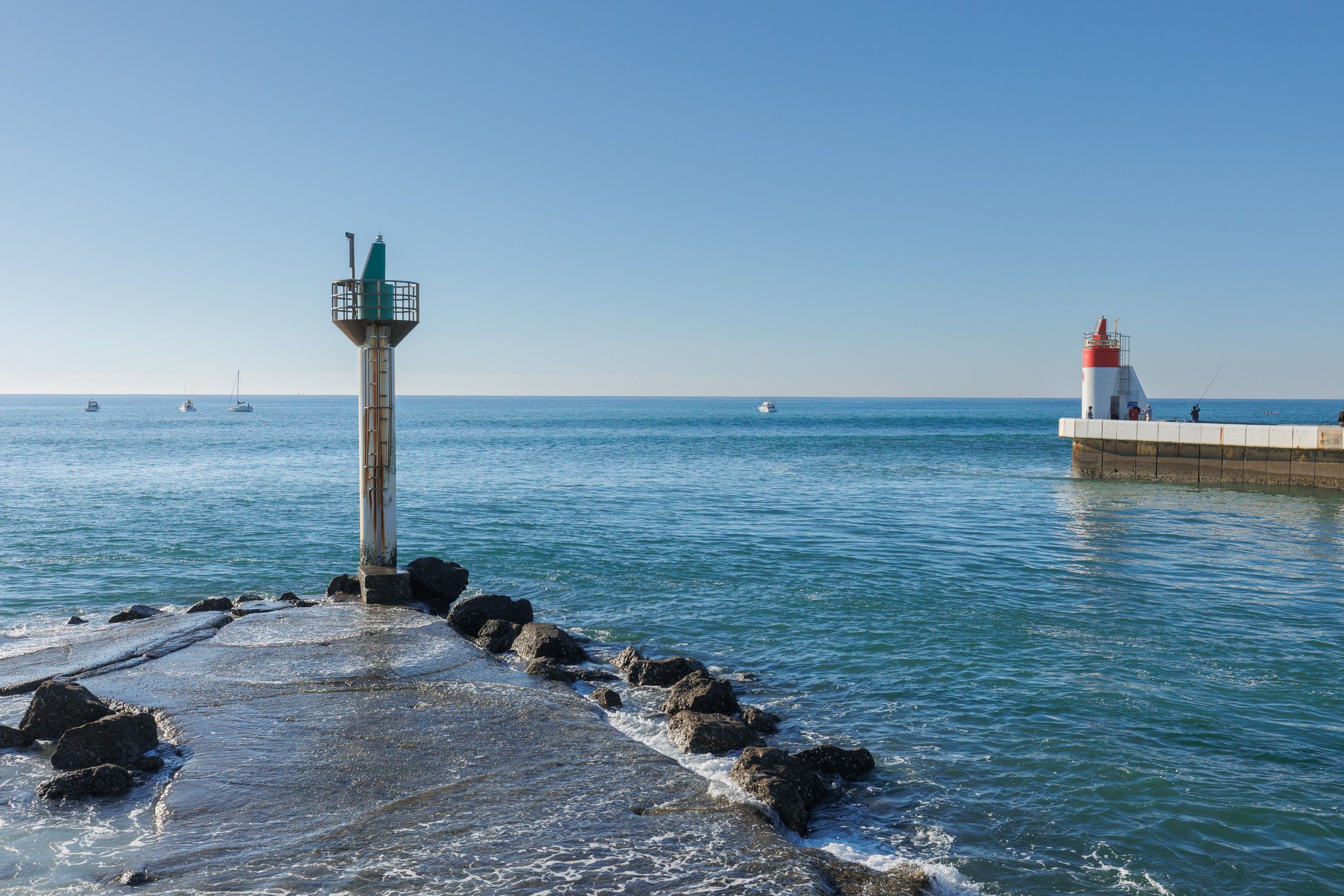 Un paysage côtier avec un phare et une jetée qui s’avance dans l’eau.