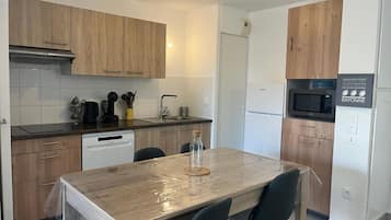 Una cocina moderna con armarios de madera, lavavajillas, microondas y una mesa con sillas.