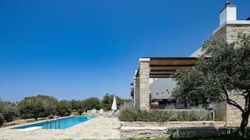 Un edificio de piedra con piscina, mobiliario exterior y olivos.