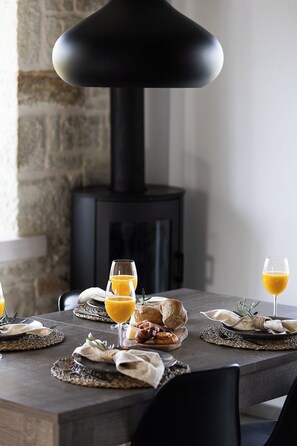 Une table à manger dressée avec des assiettes, des verres, du pain et un panier à pain, le tout éclairé par un luminaire suspendu au design moderne.