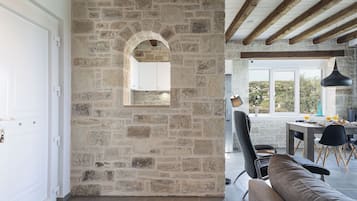 A stone-walled room with a wooden ceiling, a dining area with a table and chairs, and a view of the outdoors.