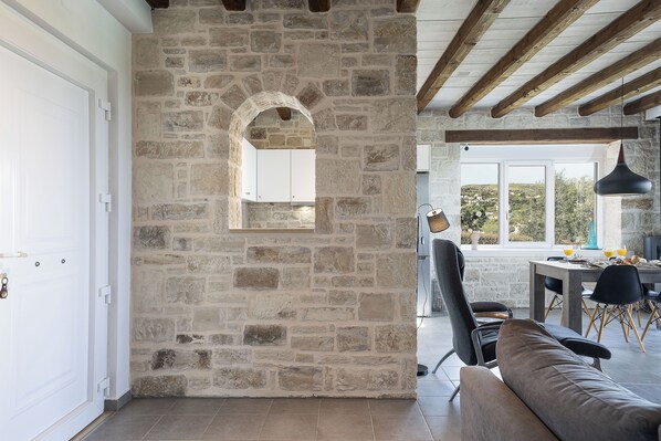 Une pièce aux murs de pierre et au plafond en bois, comprenant un coin repas avec une table et des chaises, et offrant une vue sur l’extérieur.