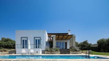 Una casa moderna de dos pisos con piscina, patio cubierto y pared de piedra.