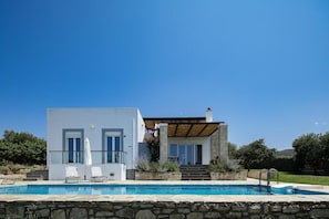 Una casa moderna de dos pisos con piscina, patio cubierto y pared de piedra.