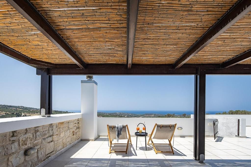 A covered outdoor seating area with two chairs and a table, overlooking a scenic view.