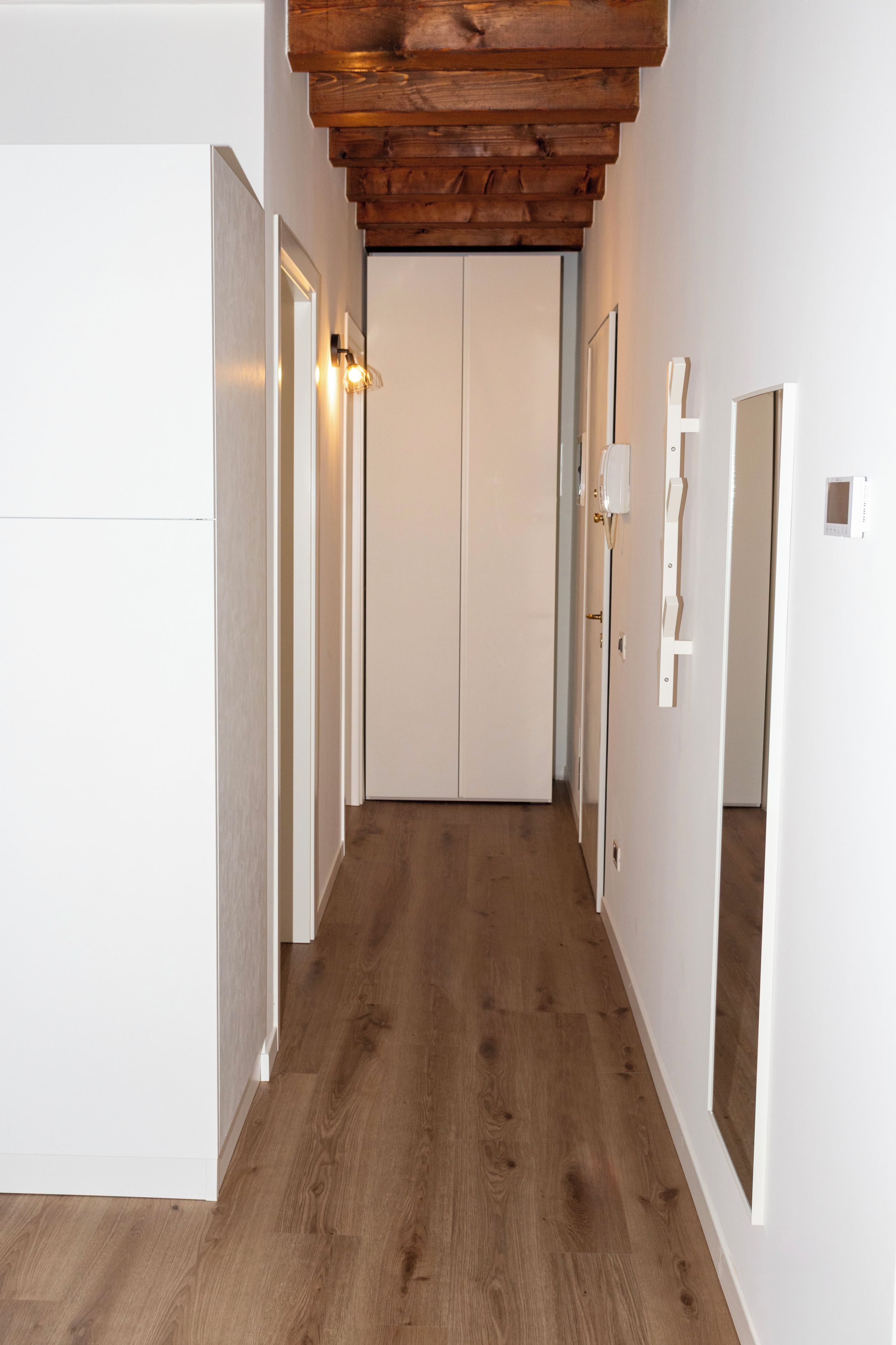 Ein Flur mit Holzboden, weißen Wänden und einer Tür am Ende.