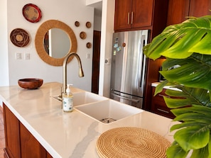 A kitchen with a stainless steel refrigerator, a wooden bowl on the counter, and a large green plant. - Villa 33 | Tropical Retreat at Villas Sol (Playa Hermosa)