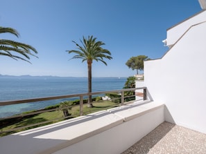 A balcony with a view of the sea, a palm tree, and a white building. - Sun of Alcanada Apartment with sea views (Alcanada)