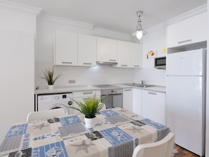A modern kitchen with white cabinetry, a built-in oven, a dishwasher, and a refrigerator. - Sun of Alcanada Apartment with sea views (Alcanada)