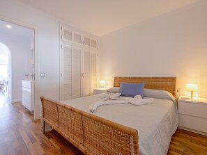 A bedroom with a bed, bedside tables, a wardrobe, and a wicker bench. - Sun of Alcanada Apartment with sea views (Alcanada)