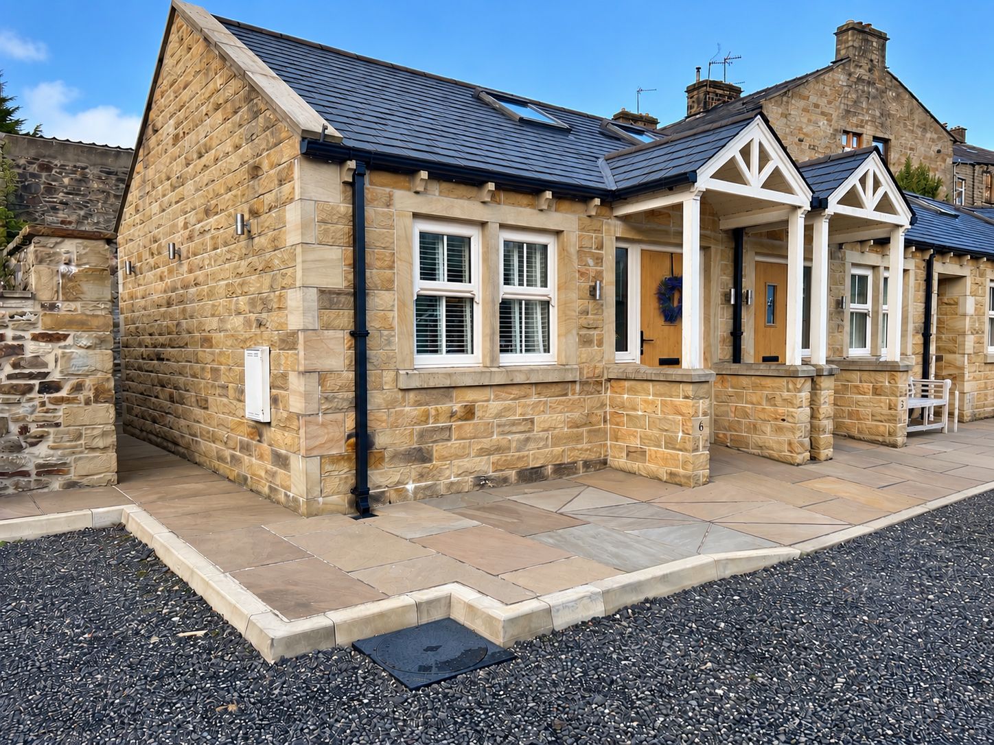 A stone building with a gabled roof, a front door, and a bench outside.