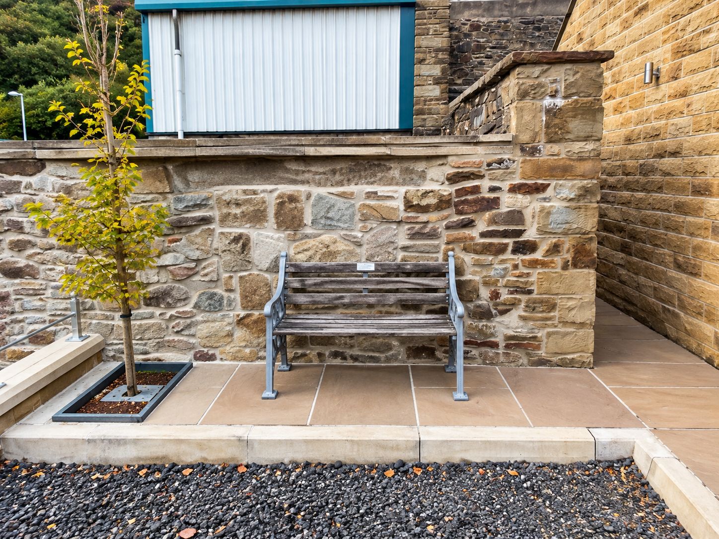 A stone wall with a bench and a tree in front.