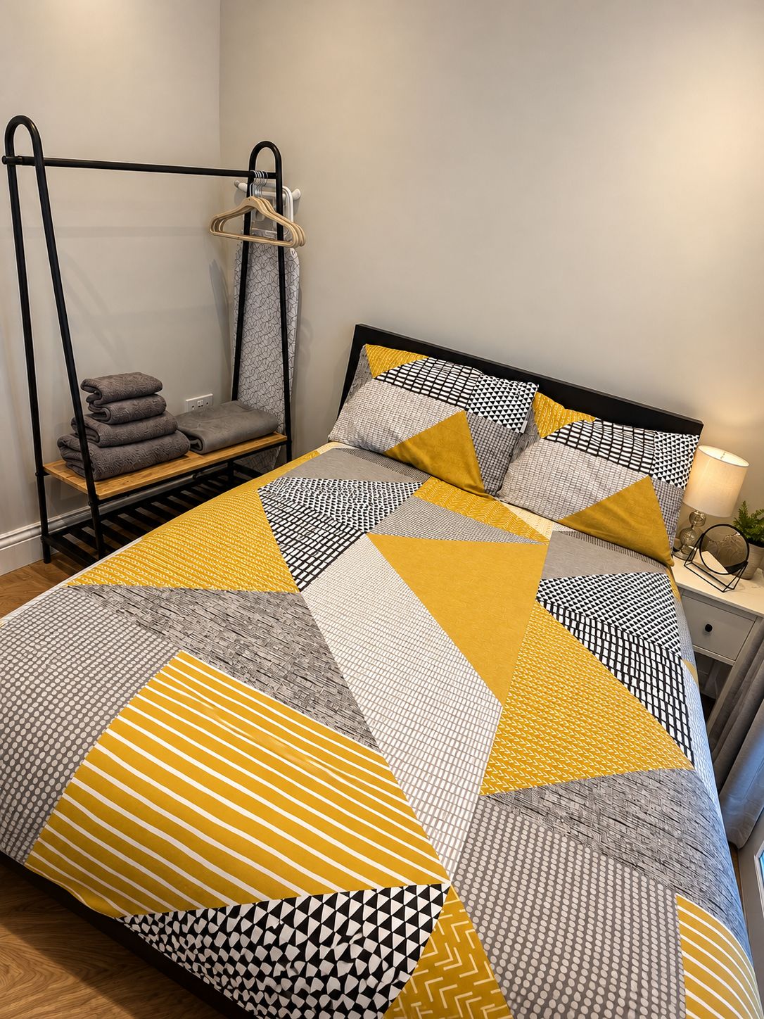 A bed with a geometric patterned bedspread and pillows, a bedside table with a lamp, and a hanging chair with towels.