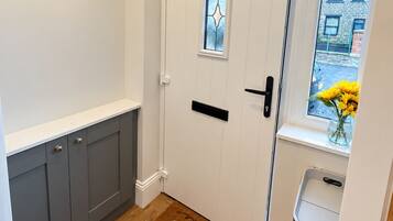 A hallway with a wooden floor, a white door with a glass window, a coat rack, and a trash bin.