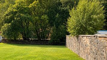 A grassy area with a stone wall and metal railings, likely part of a park or garden setting.